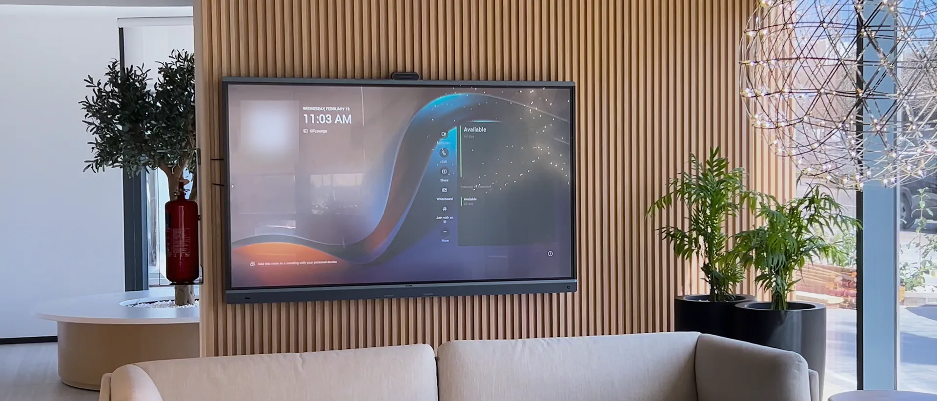 A Microsoft Teams Rooms display on a timber-slat wall in an office lounge in Amman